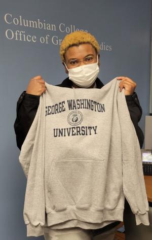 Dominique White posing with the sweatshirt she won during the CCAS Office of Graduate Studies Valentine's Week Raffle.