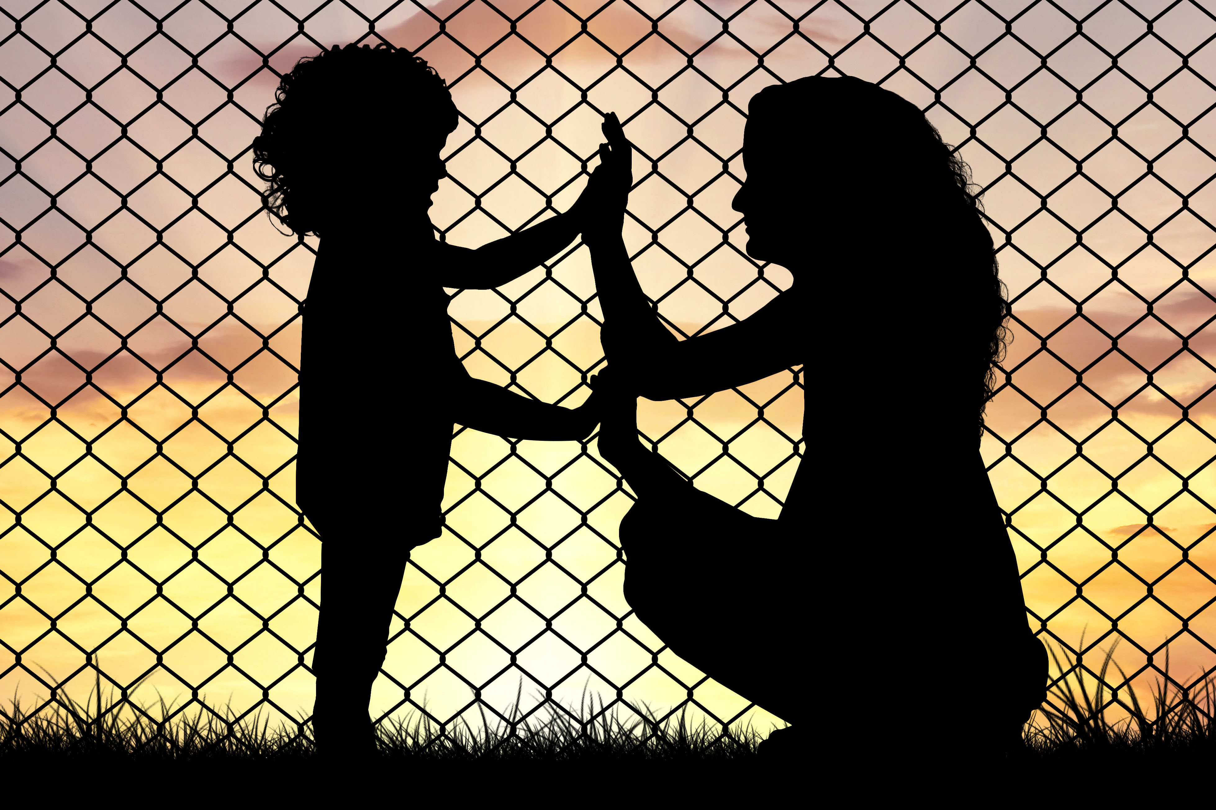Image of mother and daughter silhouettes holding hands in front of a fence.