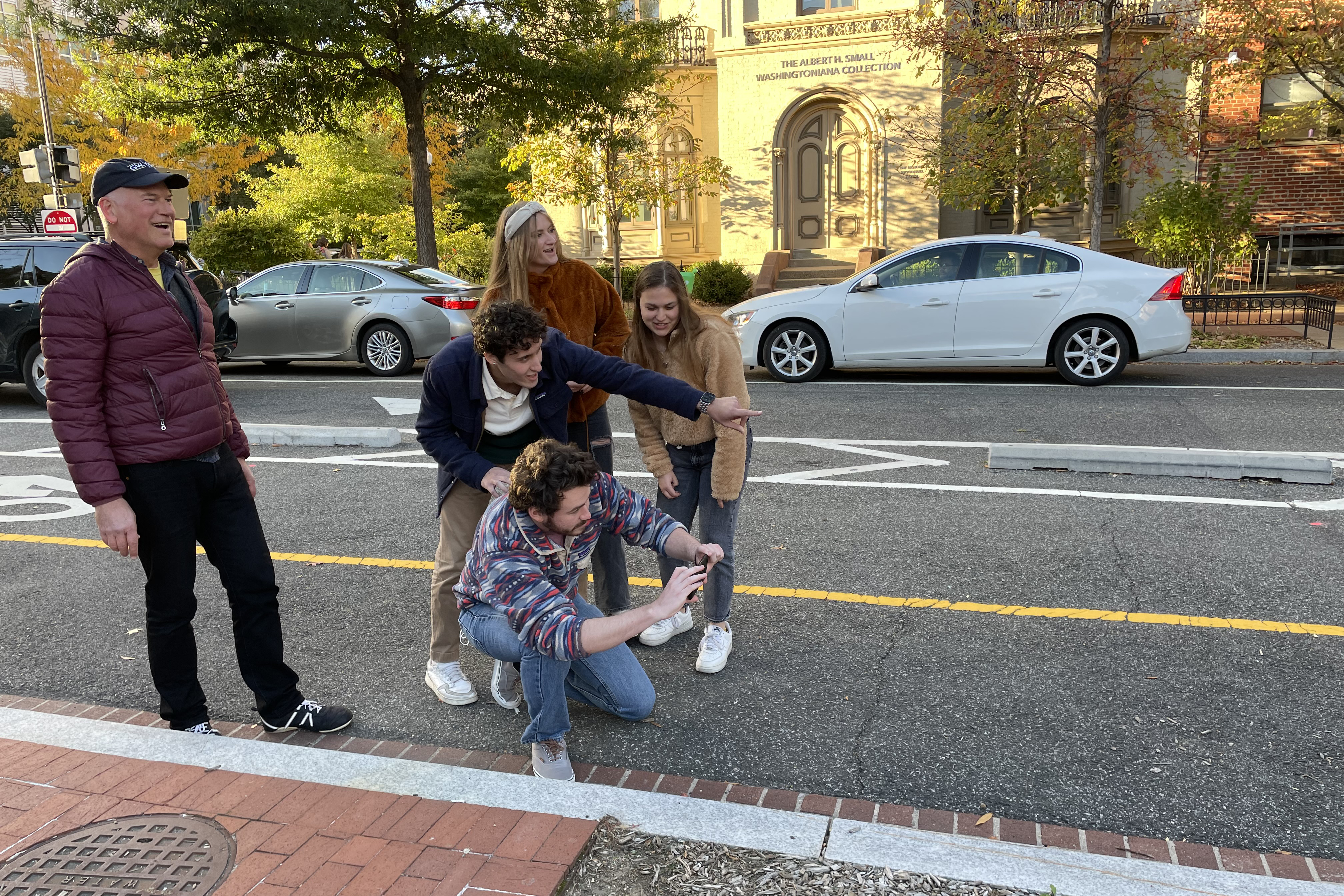 Students in a parking lot crouch around an iPhone