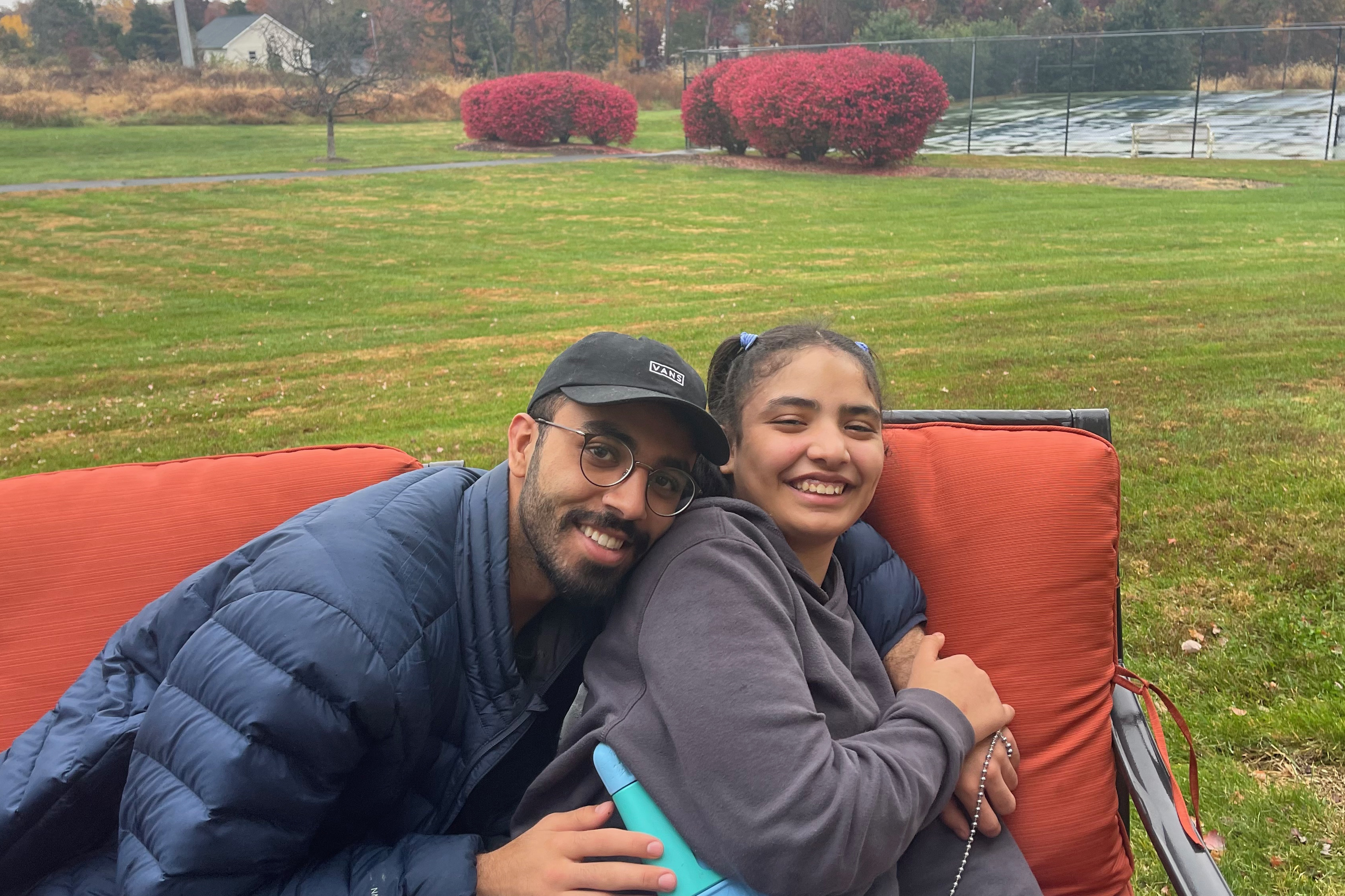 Mohammed and his sister embrace on a couch outdoors