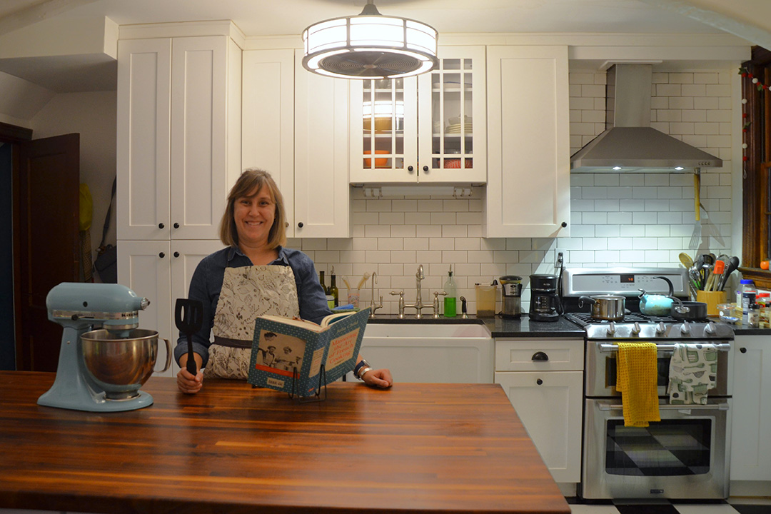Caroline J. Smith in her kitchen surrounded by cookware and holding her book