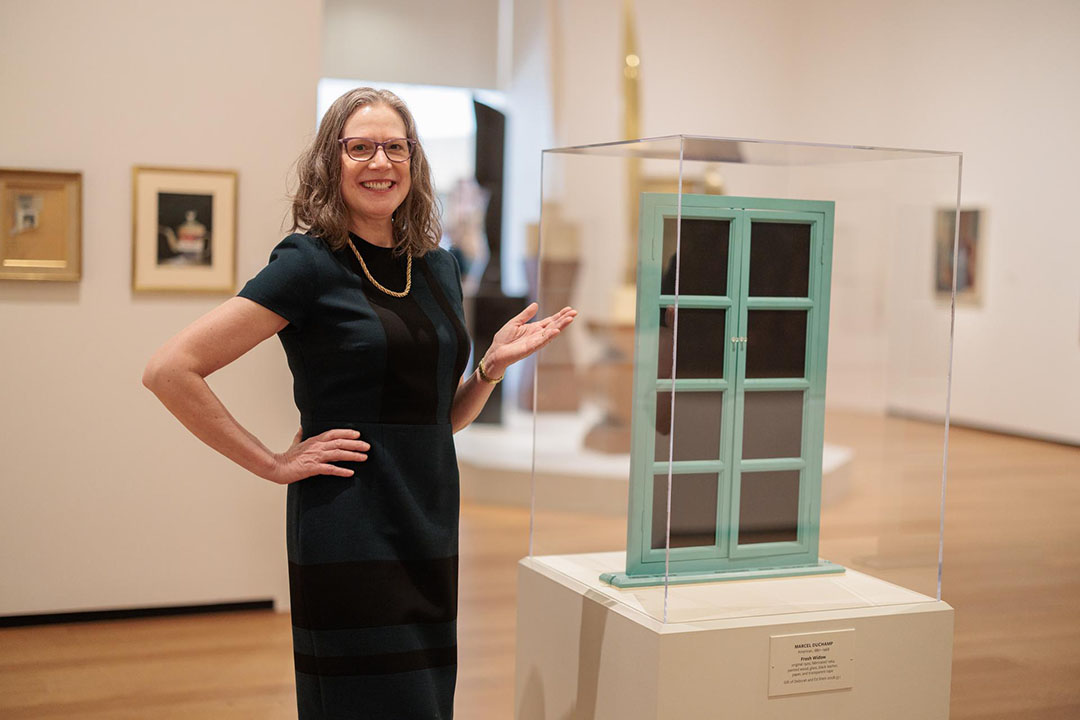 Lisa Lipinski standing in a white gallery next to a sculpture of green windowed doors