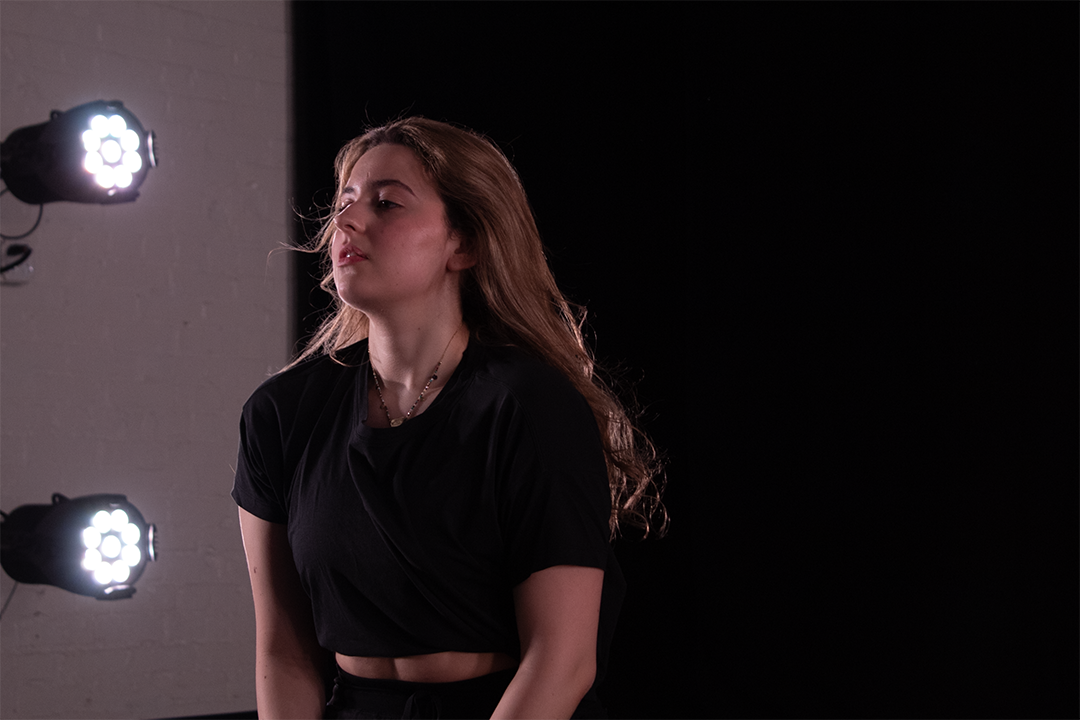 Alexia Papatsa standing on a stage-like background with lights