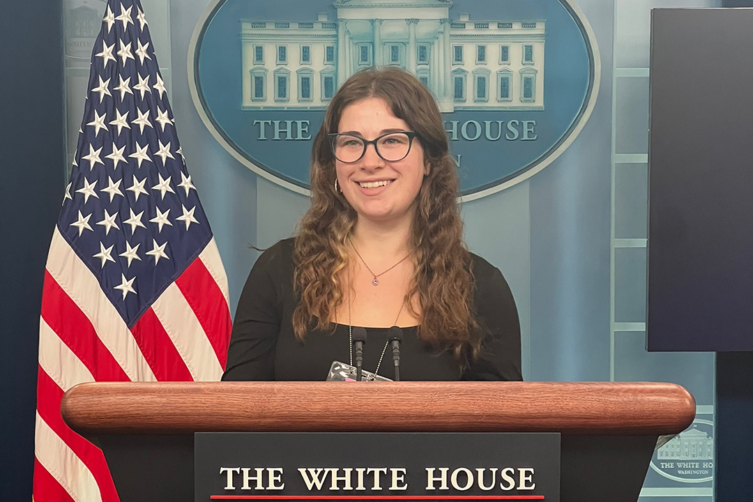 Katrina Hauser standing at a podium at the White House with an American flag and White House seal