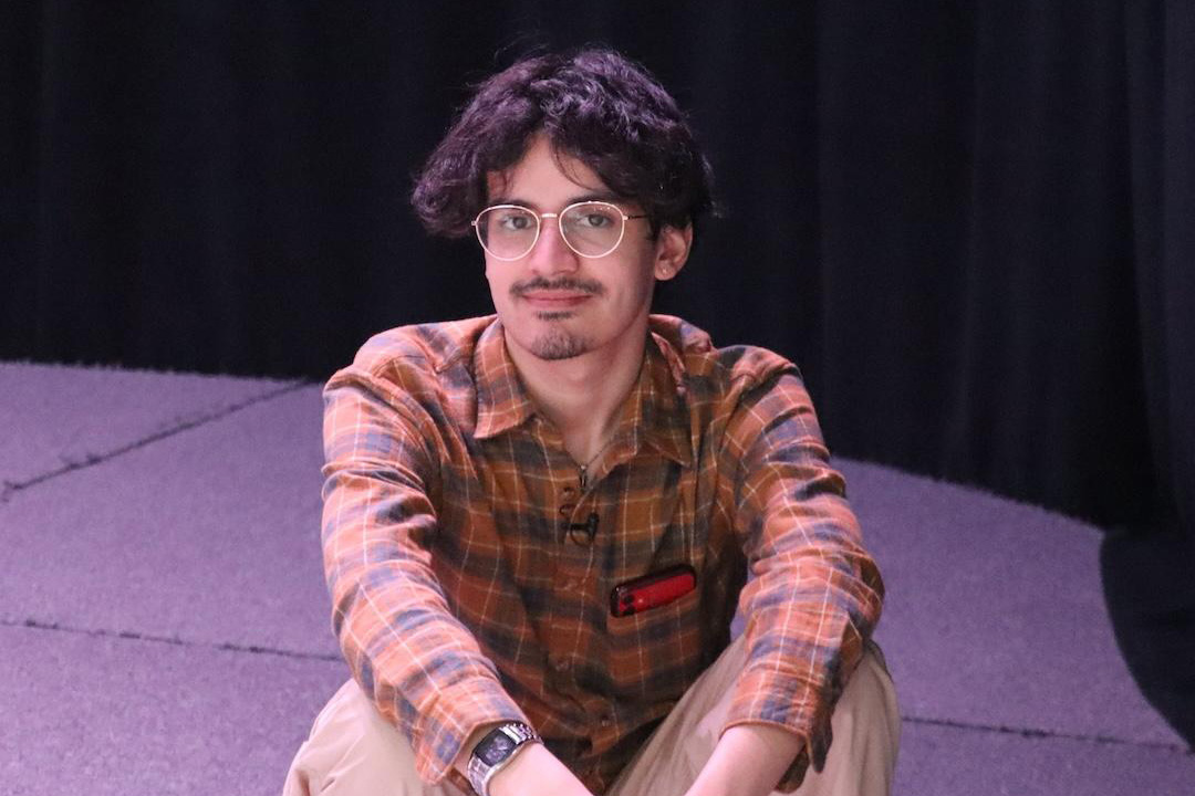 Nicholas Anastácio sitting on a stage lit with purple lights