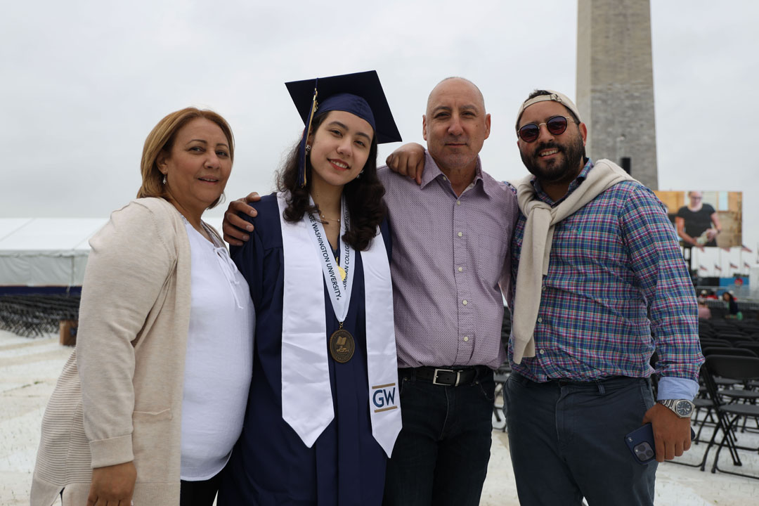 A graduate in cap and gown with three family members and the Washington Monument in the background