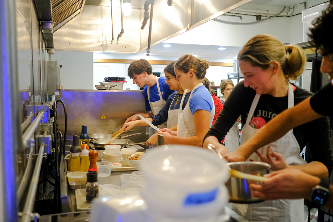 A group of students standing in a kitchen wearing white aprons and cooking
