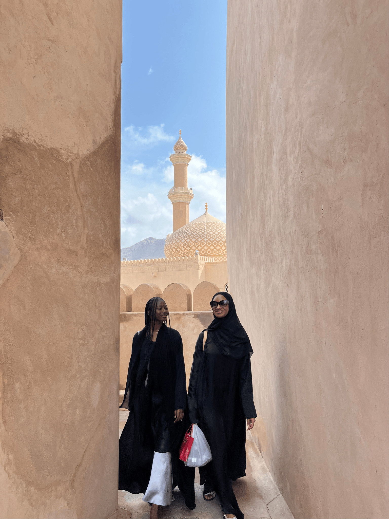 Students walk through narrow alley, with a minaret and mountains framed in the background.