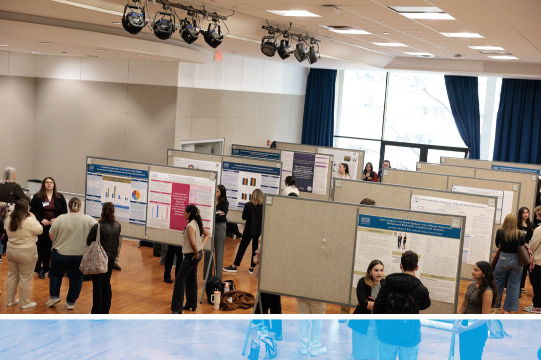 Students discuss presentations posted on wallboards throughout large hall