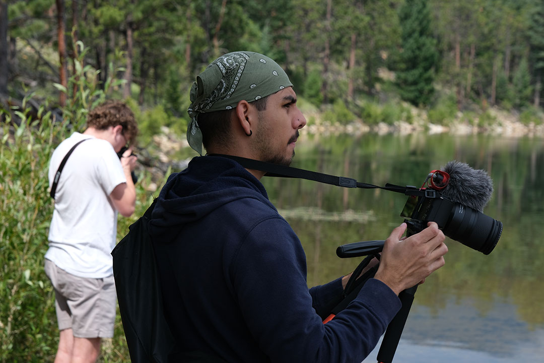 Nicholas Zafiro holding a camera outside by a lake