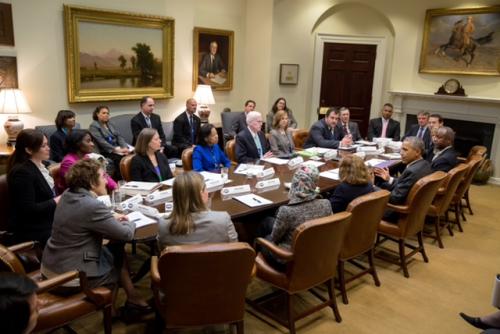 Federal administrators sitting around an oval tabling and discussing with former President Barack Obama