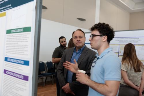 Christopher Petrarca discusses his research at a wallboard with CCAS Dean Paul Wahlbeck looking on