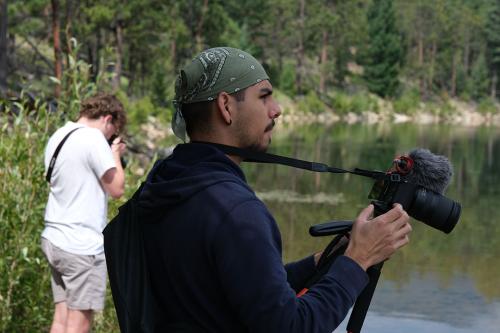 Nicholas Zafiro holding a camera outside by a lake