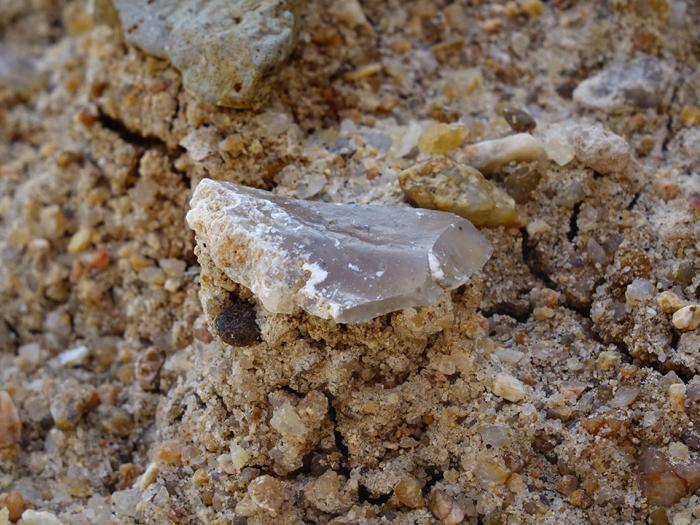 Close up of a stone tool sitting in a patch of sandy dirt