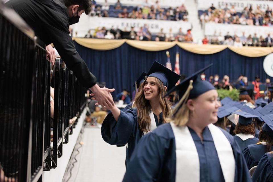 A young woman in cap and gown shakes hands with someone over a barrier.