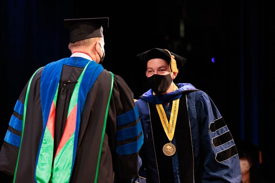 Dean Paul Wahlbeck shaking hands with a doctoral graduate on stage