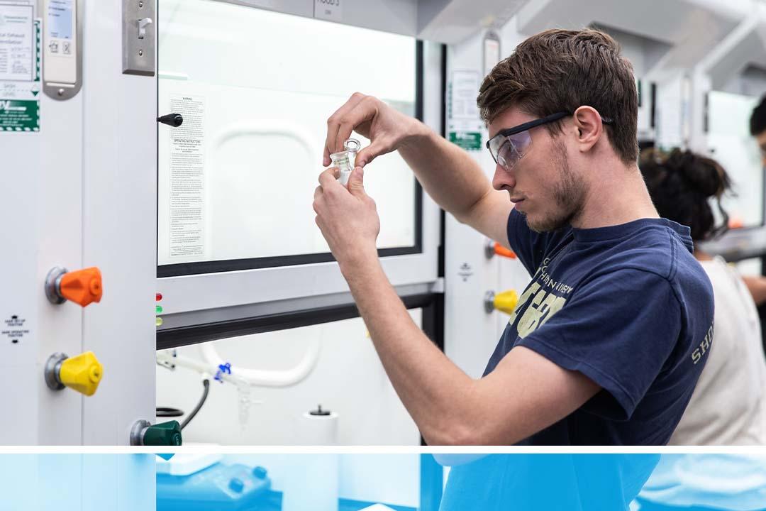 An undergraduate chemistry student in goggles holding up test tubes in a lab