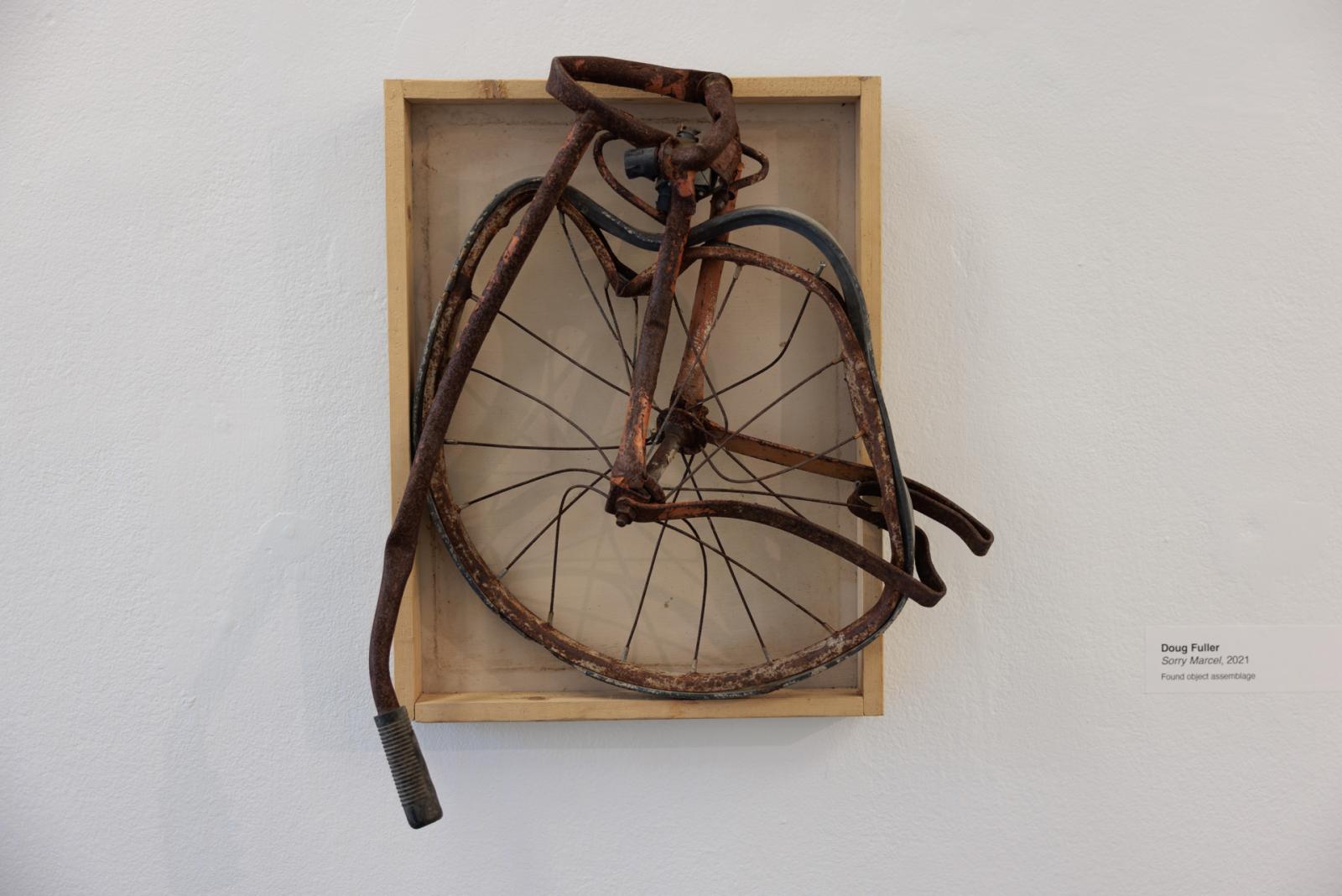 "Sorry Marcel" by Doug Fuller depicts a crushed bike collapsed into a box