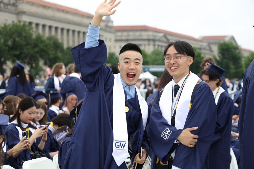 Two recent graduates on the National Mall in caps and gowns, one with his fist in the air