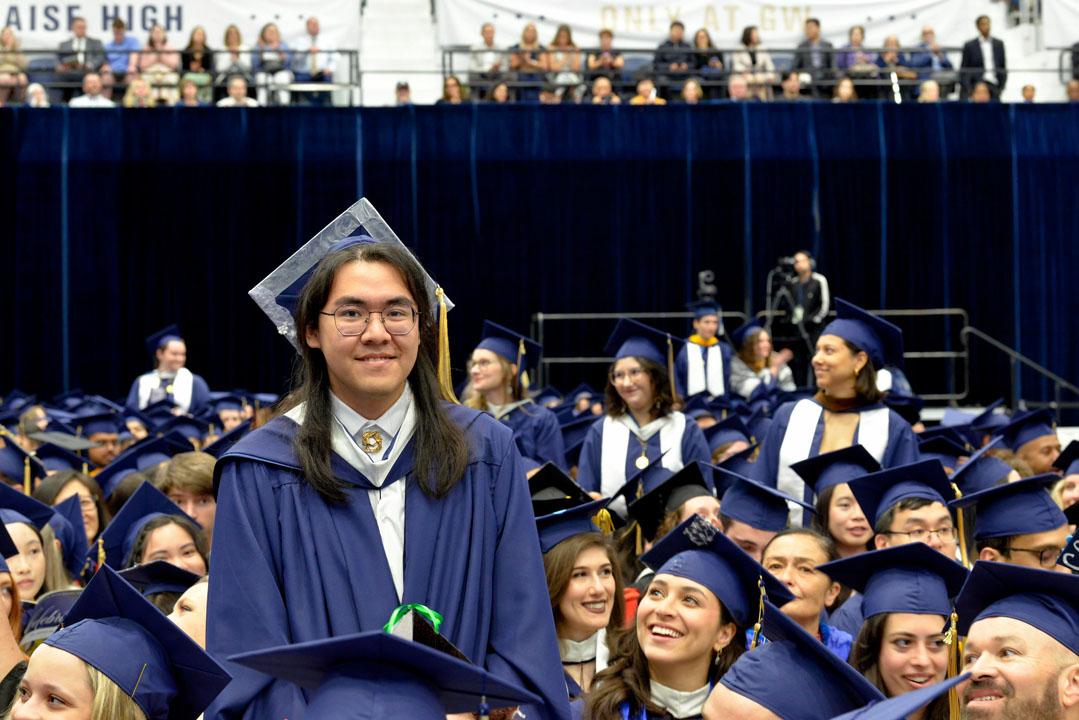A student in a cap and gown standing among a crowd of graduates