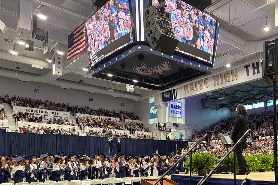 A crowd of undergraduate students facing a stage in the Smith Center, wearing caps and gowns at GW's 2025 undergraduate celebration