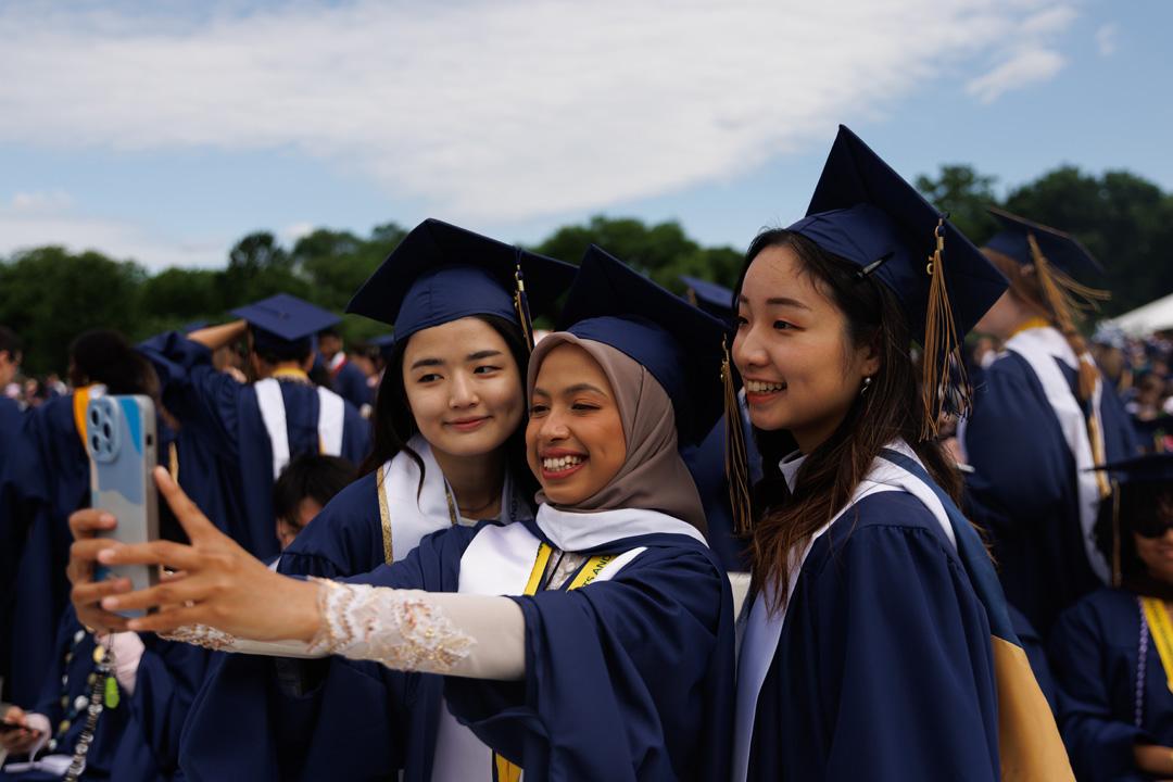 Three GW CCAS students in graduation caps and gowns taking a selfie on the National Mall