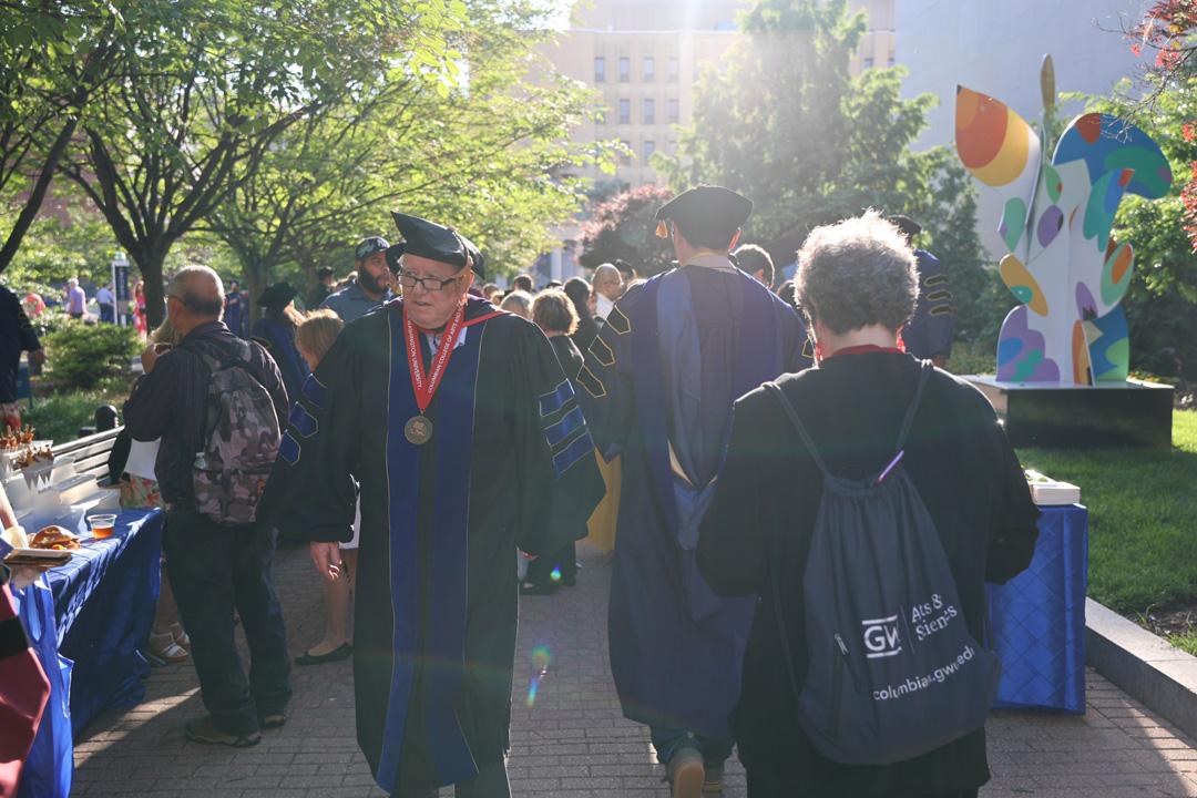 A GW graduate in doctoral regalia walking through a crowd of recent graduates outside on a sunny day