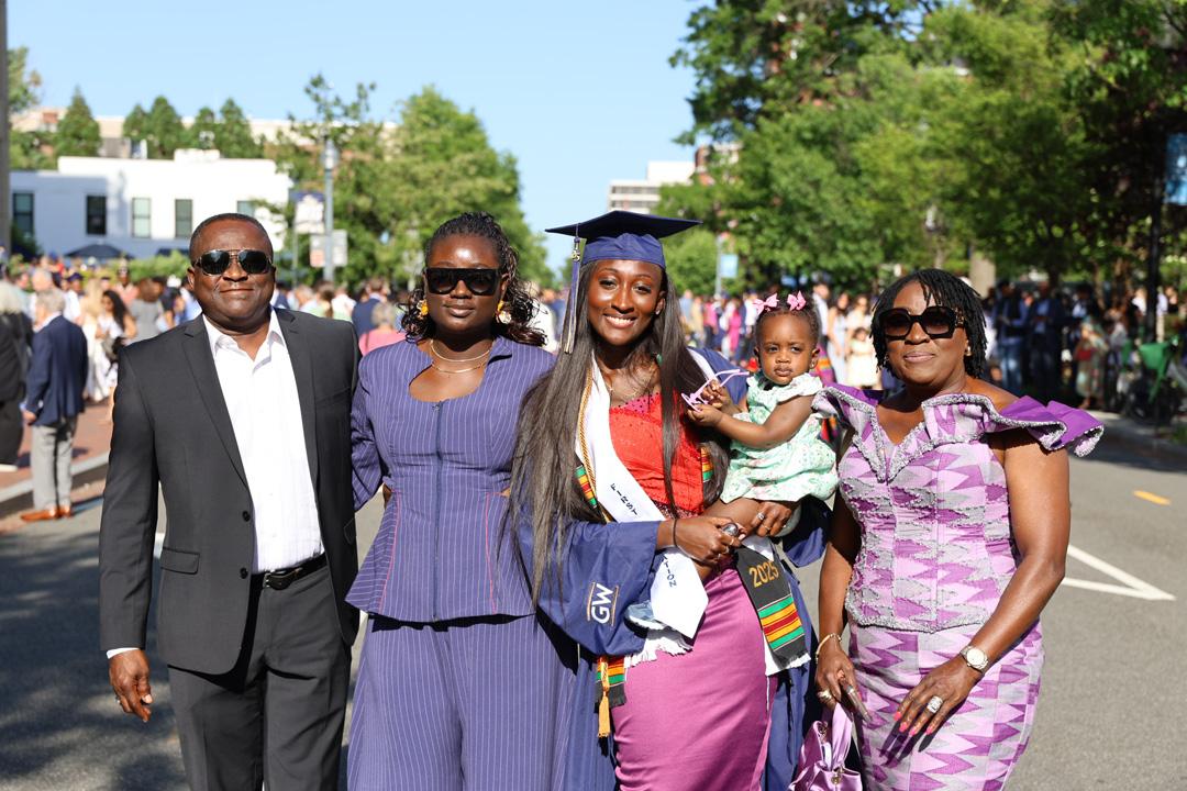 A CCAS graduate in cap and gown holding a baby and standing with her family outside after the 2025 CCAS ceremony