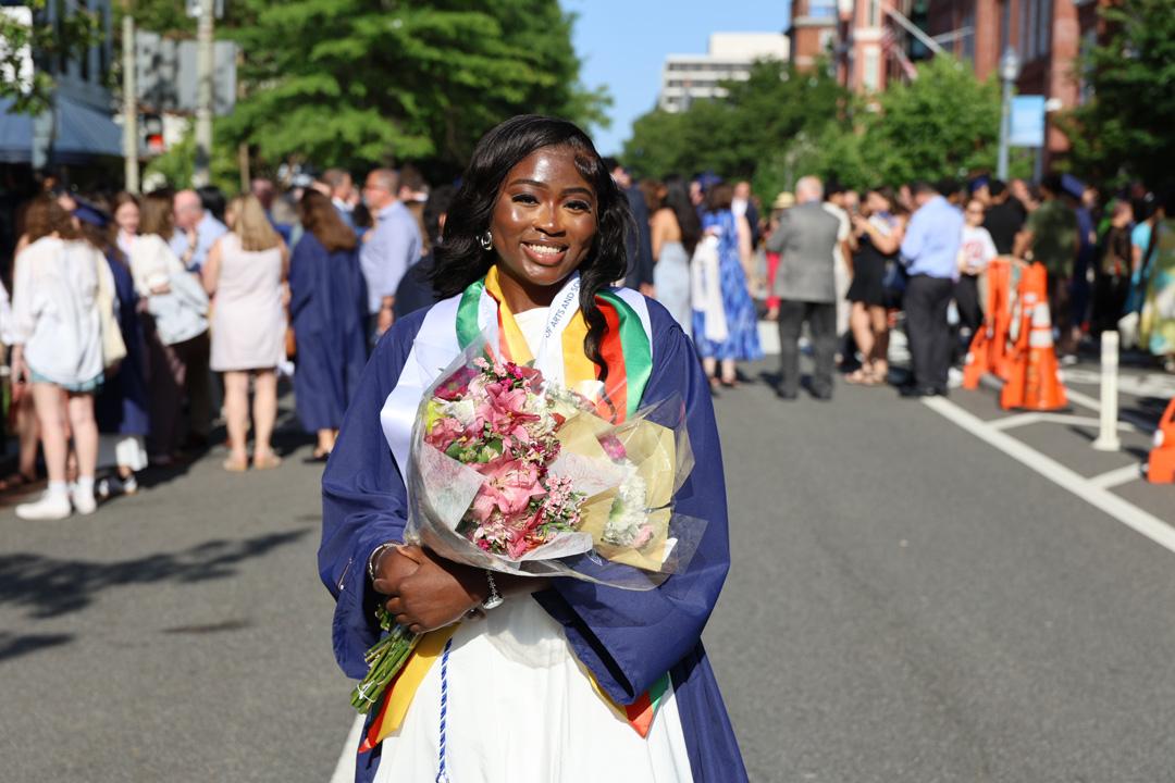 An undergraduate CCAS student holding flowers and wearing a cap and gown at the 2025 CCAS ceremony