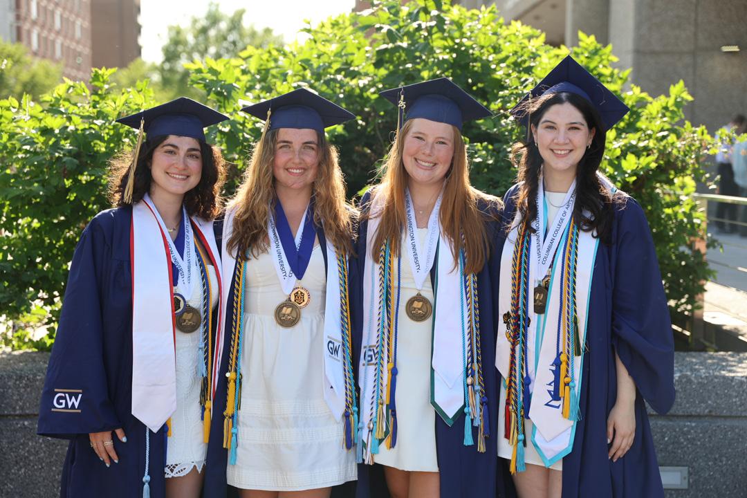 Four GW CCAS undergraduate students in graduation caps and gowns at the 2025 CCAS celebration