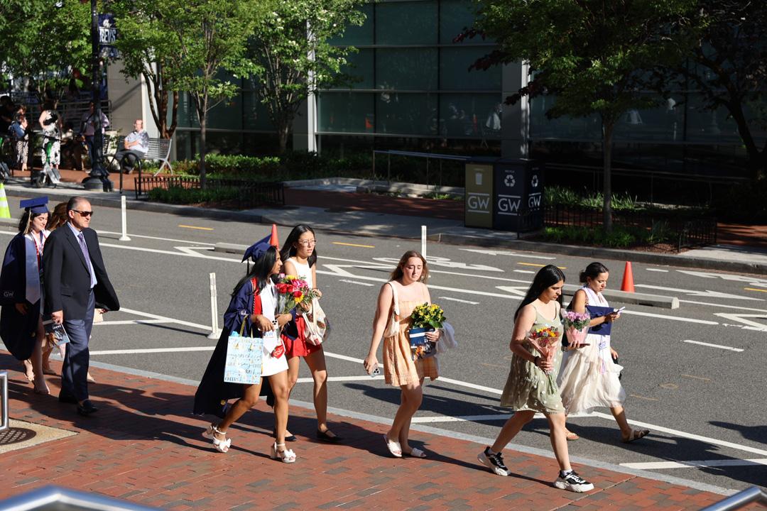 A group of CCAS graduates in caps and gowns walking down the street