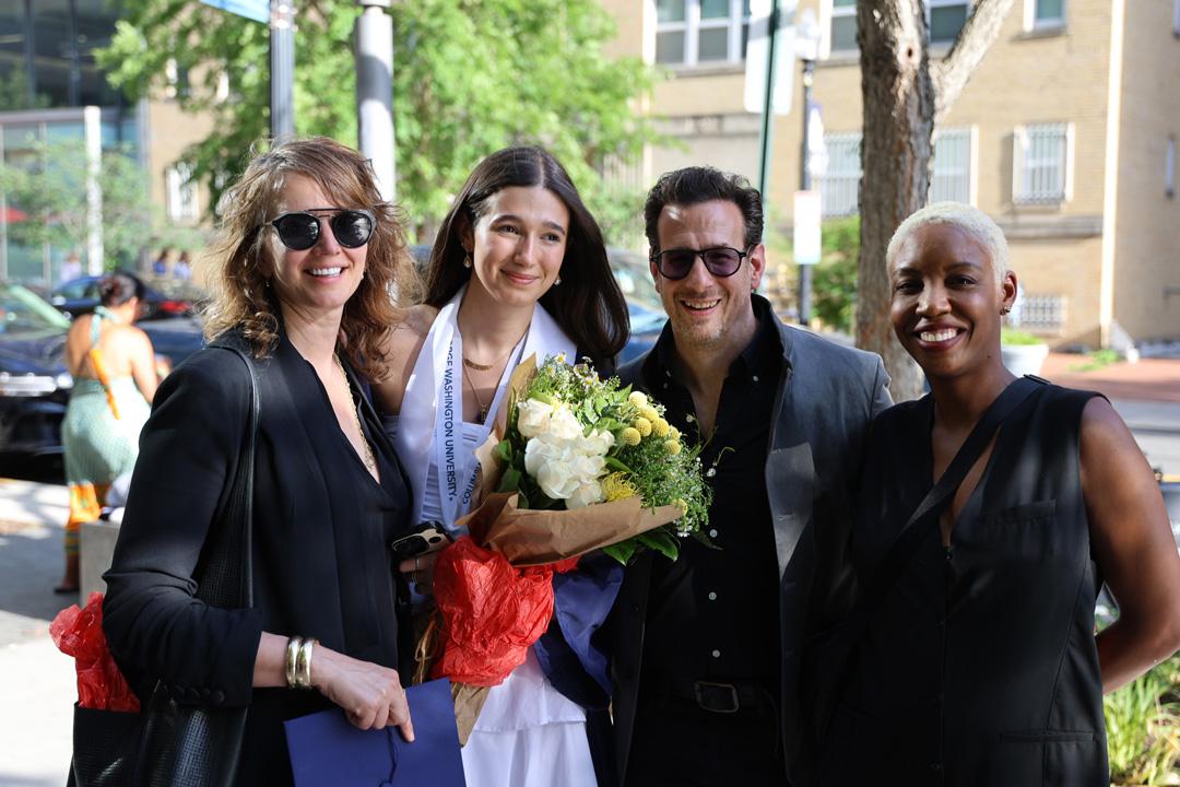 An undergraduate GW student and three other people standing together at the 2025 Columbian College undergraduate ceremony wearing caps and gowns