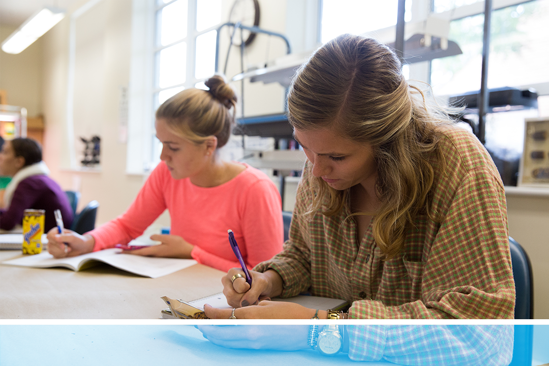 Two students bent over writing at a shared table