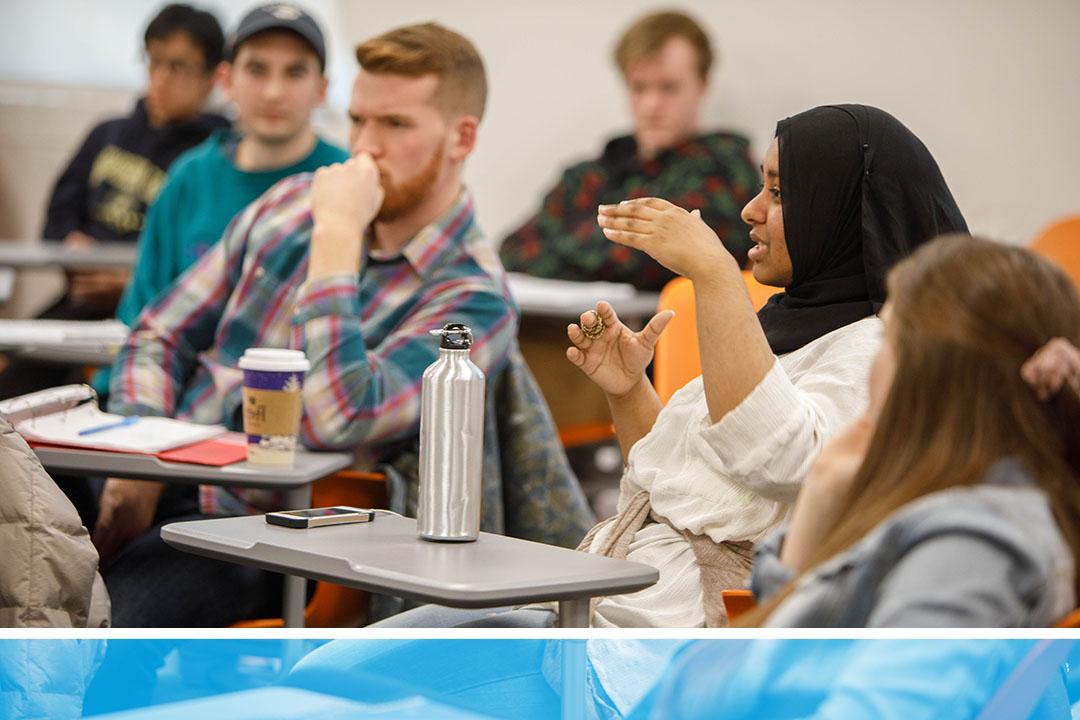 An undergraduate student wearing a head scarf speaking and gesturing in a philosophy classroom