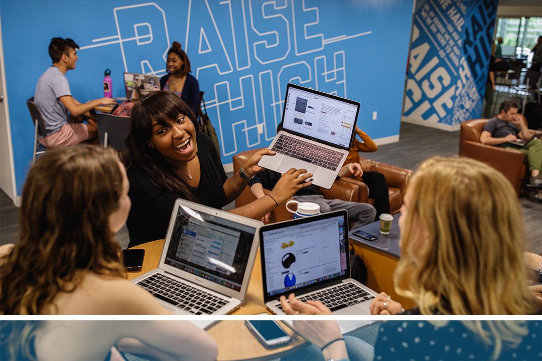 A group of students at laptops smiling and talking together
