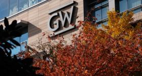 GW logo on the side of a tall brick and glass building, with trees with orange and red leaves in front